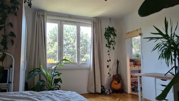 Helles Schlafzimmer mit Parkettboden, vielen Pflanzen und Blick ins Grüne durch das Fenster.