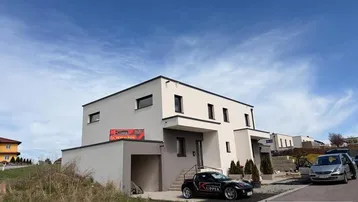 Modernes Einfamilienhaus mit Flachdach und Garage in ländlicher Umgebung unter blauem Himmel.