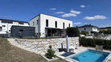 Modernes Einfamilienhaus mit Garten, Pool und Terrasse unter blauem Himmel.