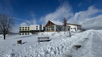Gebäudekomplex in einer verschneiten Winterlandschaft unter blauem Himmel mit einigen Bäumen.
