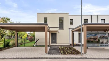 Moderne Reihenhäuser mit Carports und gepflasterter Zufahrt unter blauem Himmel.
