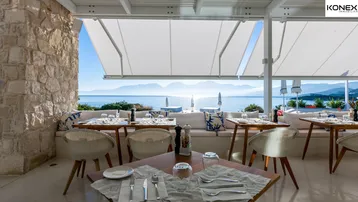 Heller Restaurantbereich mit Tischen und Stühlen, bietet einen weiten Blick auf das Meer.