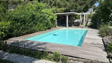 Außenbereich mit Swimmingpool und Holzdeck, umgeben von üppigem Grün und Bäumen.