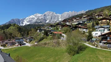 Panoramablick auf ein malerisches Bergdorf mit schneebedeckten Gipfeln im Hintergrund unter blauem Himmel.