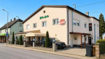 Seitenansicht des Gebäudes mit überdachter Terrasse und geparktem Fahrzeug auf dem Grundstück.