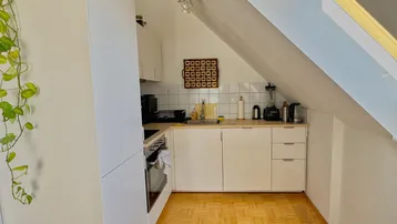 Kleine Küche mit weißen Schränken, Herd und Spüle unter einer Dachschräge.
