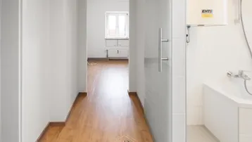 Heller Flur mit Holzfußboden, der zu einem weiteren Raum führt, mit Blick auf ein Badezimmer.
