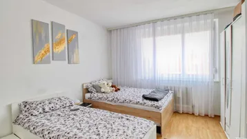 Helles Schlafzimmer mit zwei Einzelbetten, Holzfußboden und großen Fenstern mit Vorhängen.