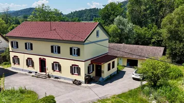 Haus mit gelber Fassade, rotem Satteldach und umgebender grüner Landschaft.