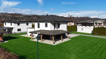 Modernes Einfamilienhaus mit großem Garten und überdachter Terrasse in ländlicher Umgebung.