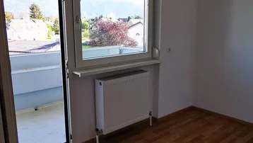 Helles Zimmer mit Laminatboden, Heizkörper und Zugang zu einem Balkon mit Bergblick.