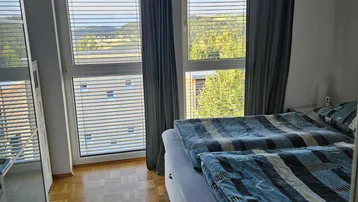 Schlafzimmer mit zwei Betten, Parkettboden und großen Fenstern mit weitem Ausblick.