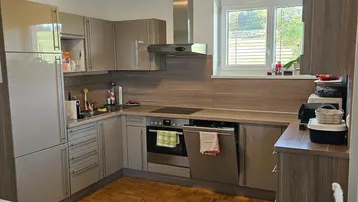 Moderne Küche mit beigen Schränken, Einbaugeräten und Fenster mit Blick ins Grüne.