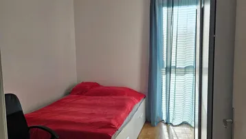 Helles Schlafzimmer mit Einzelbett, Schreibtisch und Parkettboden, durchflutet von Sonnenlicht.