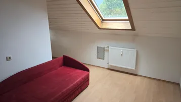 Dachschrägenzimmer mit Holzbalkendecke, Dachfenster und einem roten Schlafsofa.