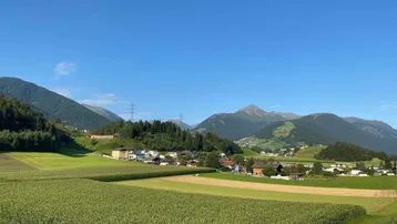 Ländliche Landschaft mit grünen Feldern, Bergen und einem kleinen Dorf unter blauem Himmel.