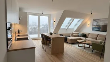 Offener Wohn-Essbereich mit moderner Küche, Holzboden, großen Fenstern und Dachschrägen.