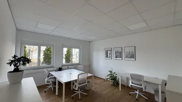 Modernes Büro mit Holzboden, weißen Wänden und mehreren Arbeitsplätzen, hell durch große Fenster.