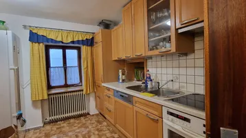 Gemütliche Küche mit Holzschränken, Fliesenboden und Fenster mit Vorhängen.