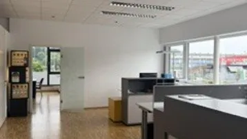 Geräumiges Büro mit Holzparkettboden, großen Fenstern und modernen Arbeitsplätzen in heller Umgebung.