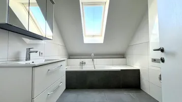 Modernes Badezimmer im Dachgeschoss mit Badewanne, Waschtisch, Spiegelschrank und Dachfenster.