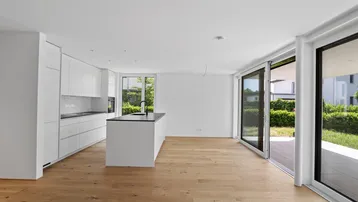 Heller, offener Wohnbereich mit moderner Einbauküche, Holzboden und Zugang zur Terrasse.
