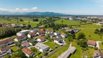Weitläufige Luftaufnahme einer Wohnsiedlung mit grünen Feldern und majestätischem Alpenpanorama im Hintergrund.