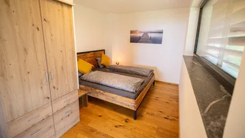 Helles Schlafzimmer mit Holzbett, Holzboden und Fenster mit Blick ins Grüne.