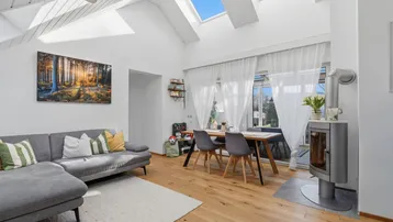 Helles Wohn-Esszimmer mit Holzboden, Kaminofen und großen Dachfenstern für viel Tageslicht.