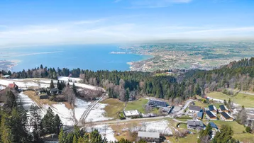 Weitläufige Landschaftsaufnahme mit See im Hintergrund und umliegenden Häusern.