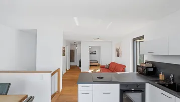 Moderne Küche mit dunkler Arbeitsplatte und Holzboden, offen zum Essbereich und Wohnzimmer.