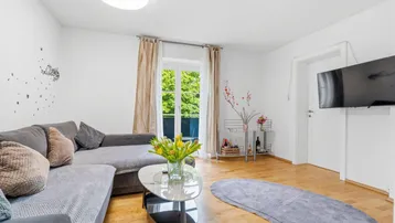 Helles Wohnzimmer mit Ecksofa, Holzboden und Zugang zu einem kleinen Balkon.