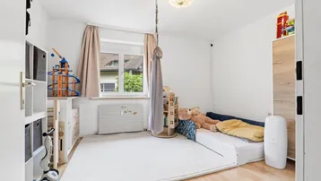 Helles Kinderzimmer mit Holzboden, Spielzeug und Fensterblick ins Grüne.