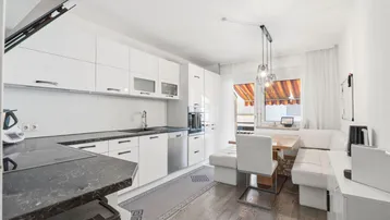 Moderne weiße Küche mit Essbereich, dunkler Arbeitsplatte und Zugang zum Balkon.