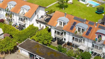 Luftaufnahme von Reihenhäusern mit Gärten, Balkonen und Solaranlagen auf den Dächern.