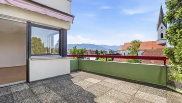 Geräumige Terrasse mit Fliesenboden, Markise und weitem Blick auf die Kirche und die Berge.