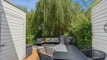 Gemütliche Terrasse mit Essbereich und Lounge-Möbeln unter einem großen Weidenbaum im Garten.