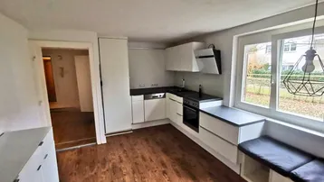 Moderne Küche mit weißen Schränken, dunkler Arbeitsplatte und integrierter Sitzbank am Fenster.