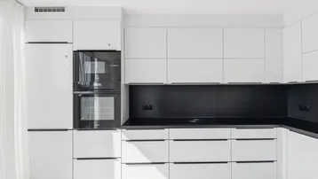Moderne, helle Küche mit weißen Schränken, schwarzen Arbeitsplatten und integrierten Geräten.