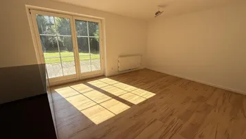 Helles Zimmer mit Laminatboden und großen Fenstern, die viel Sonnenlicht hereinlassen und Zugang zum Garten bieten.