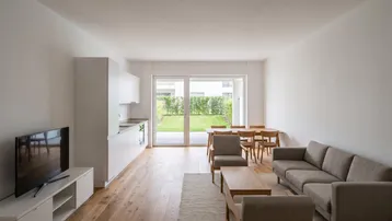 Helles, offenes Wohn-Esszimmer mit integrierter Küche, Holzboden und Zugang zum Garten.