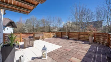 Große, sonnige Terrasse mit Holzzaun, verschiedenen Bodenbelägen und Sitzgelegenheiten im Freien.