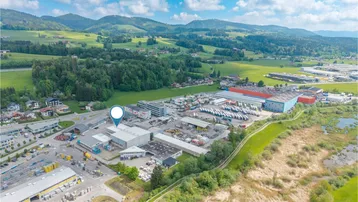 Luftaufnahme eines Industriegebiets mit grüner Landschaft und Bergen im Hintergrund, inklusive Standortmarkierung.