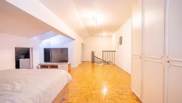 Geräumiges Schlafzimmer mit Parkettboden, Fernseher und offenem Zugang zur Treppe.