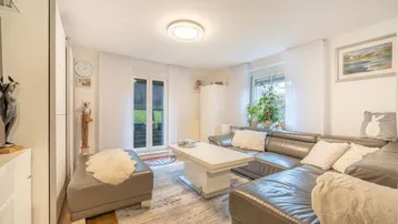 Helles Wohnzimmer mit bequemer Ledercouch, Holzboden und Zugang zum Außenbereich.