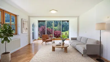 Helles Wohnzimmer mit Holzboden, bequemen Möbeln und weitem Blick ins Grüne durch große Fenster.