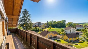 Geräumiger Holzbalkon mit traditionellem Geländer und weitem Blick über die grüne Landschaft.