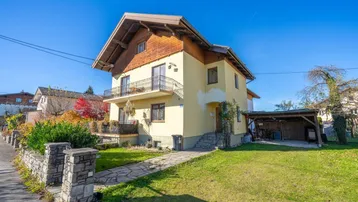 Freistehendes Einfamilienhaus mit Satteldach, Balkonen und einem Carport auf einem sonnigen Grundstück.