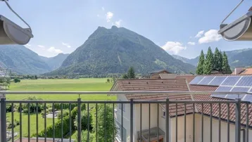 Balkon mit weitem Blick auf die umliegende Berglandschaft und grüne Felder.