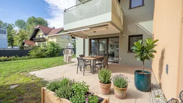 Große gepflasterte Terrasse mit Gartenmöbeln, Kräuterbeeten und Zugang zum Rasenbereich.